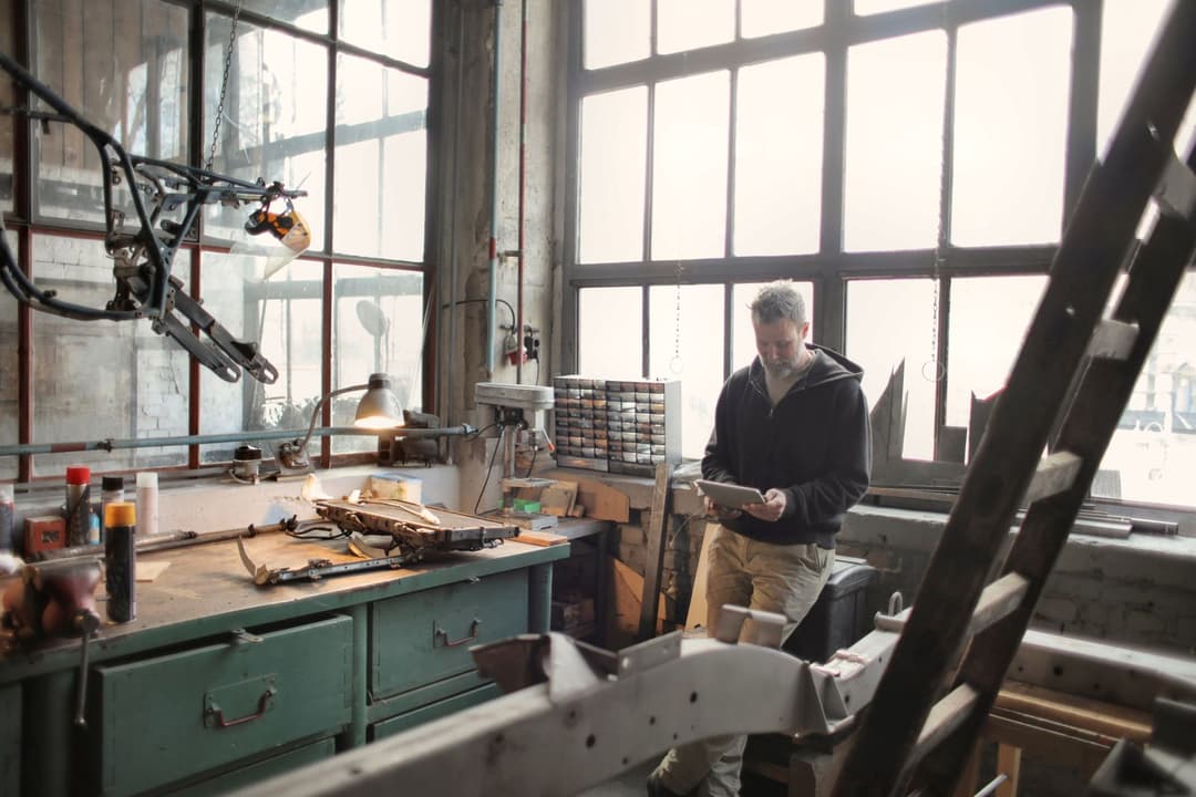Ein Mechaniker steht am Fenster seiner Werkstatt und arbeitet auf einem Tablet