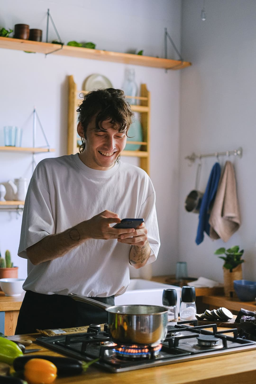 Ein Mann steht zu Hause in der Küche und schaut lächelnd auf sein Smartphone